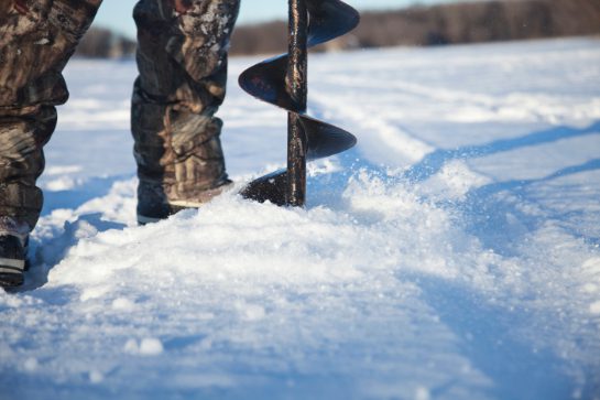 ice fisherman drilling hole in ice with auger