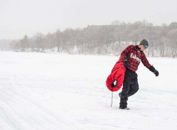 fisherman in red flannel walking to skid house on ice in daylight