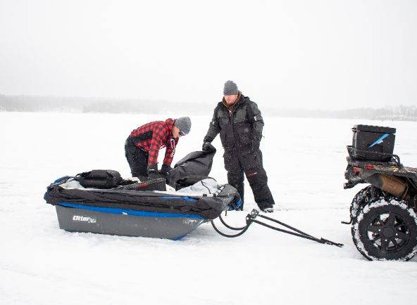 two ice fisherman unpacking a sled on ice to go ice fishing
