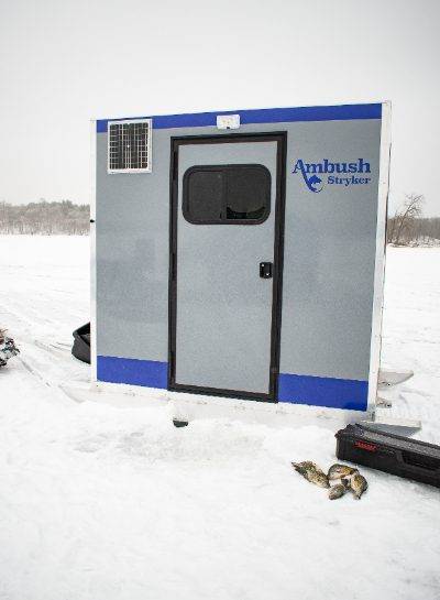 Stryker ice house on ice with fish on ice in front of it