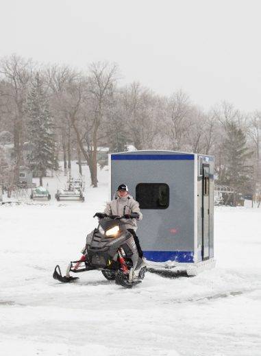 man riding snowmobile on ice pulling a blue stryker skid ice house onto the ice 